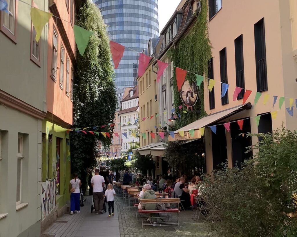 Wagnergasse in Jena mit Außengastronomie, bunten Wimpeln und Blick auf den JenTower